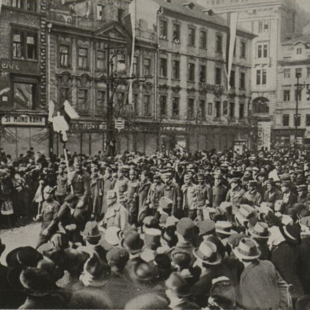 Black and white picture of crowds in Prague on 30 October 1918. Crowds are lining the street and in the middle soldiers are marching through. The crowds are in Prague's St Wenceslas Square.