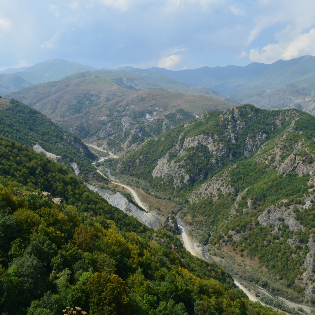 A scenic view of a winding river cutting through green, forested mountains under a partly cloudy sky.