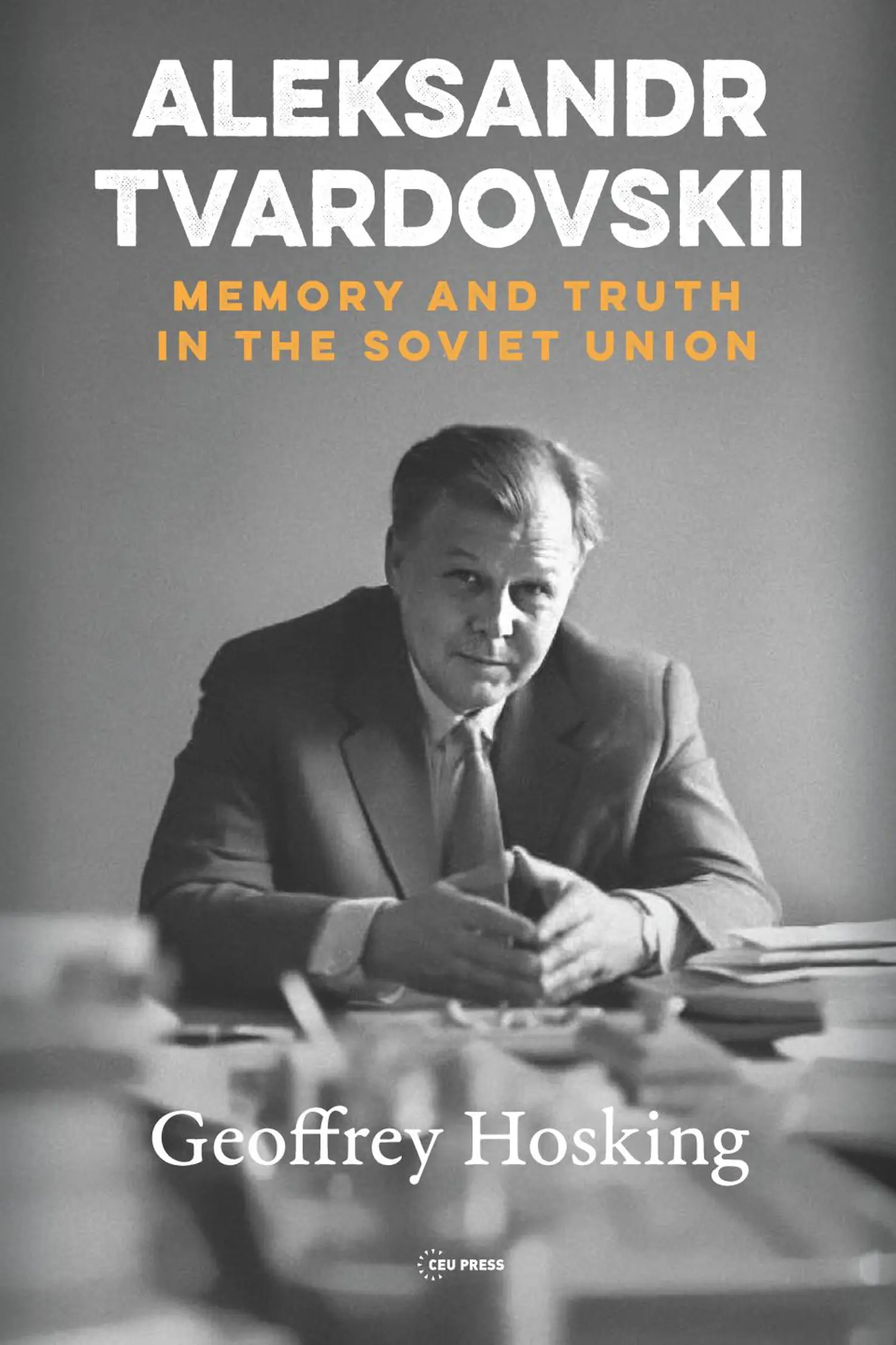 The cover features a black-and-white photograph of a man seated at a desk, dressed in a suit and tie, looking directly at the camera. The title is displayed in bold white text at the top, with the subtitle in orange, and the author's name in white at the bottom.