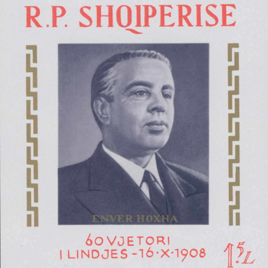 Albanian postage stamp commemorating the 60th anniversary of the birth of Enver Hoxha. The stamp features a formal black-and-white portrait of a middle-aged man in a dark suit and tie, shown in three-quarter profile against a plain background. The portrait is framed by decorative gold geometric borders on either side.